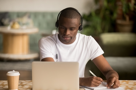 Focused man wearing headphones watching webinar training making notes study online food safety training learning language on computer